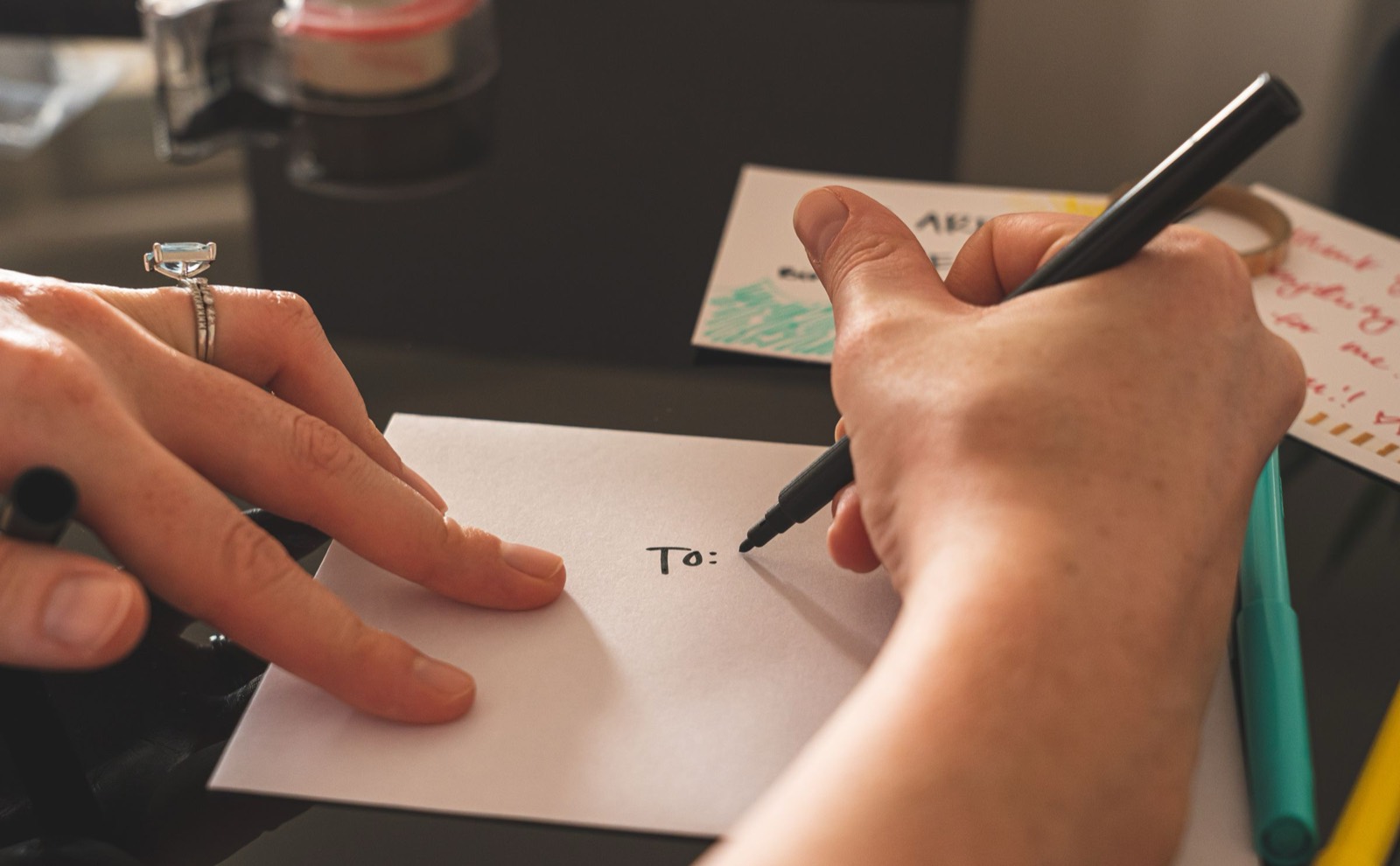 Hands addressing a white envelope with a black marker on a desk