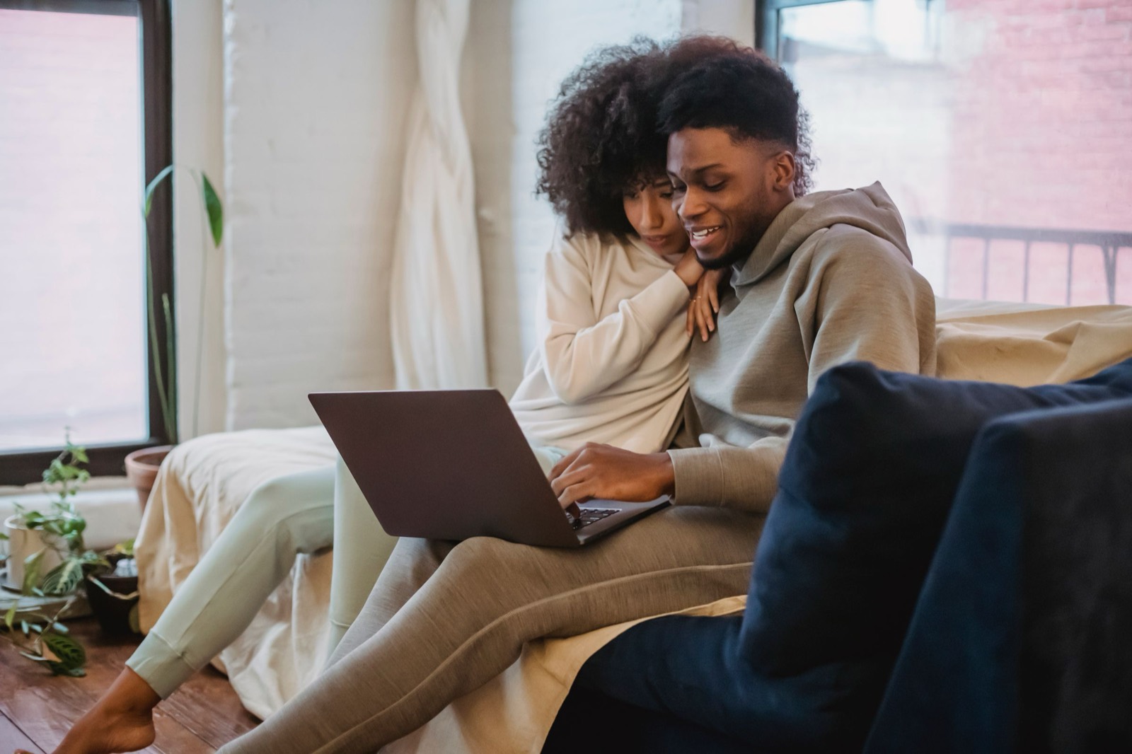 Couple relaxing on a sofa by a sunny window, sharing a laptop