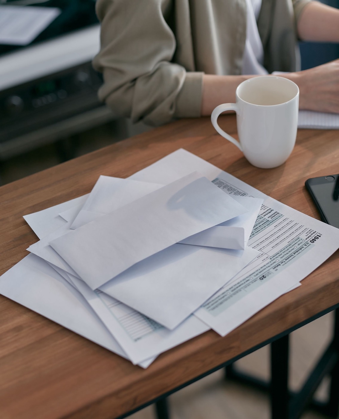 White envelopes and a blank tax form on a wooden kitchen table beside a coffee mug