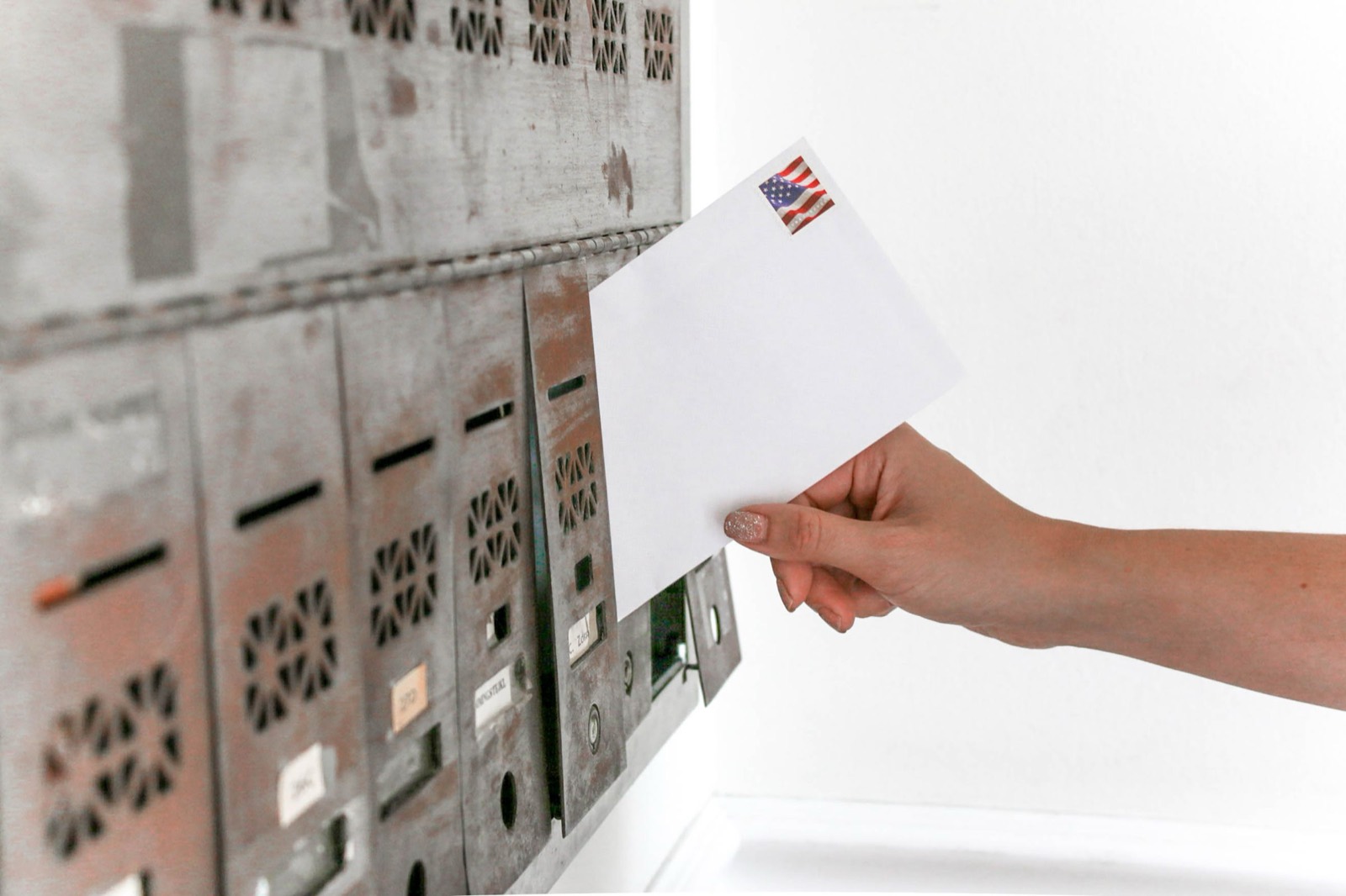 Hand dropping a stamped white envelope into a metal wall mailbox