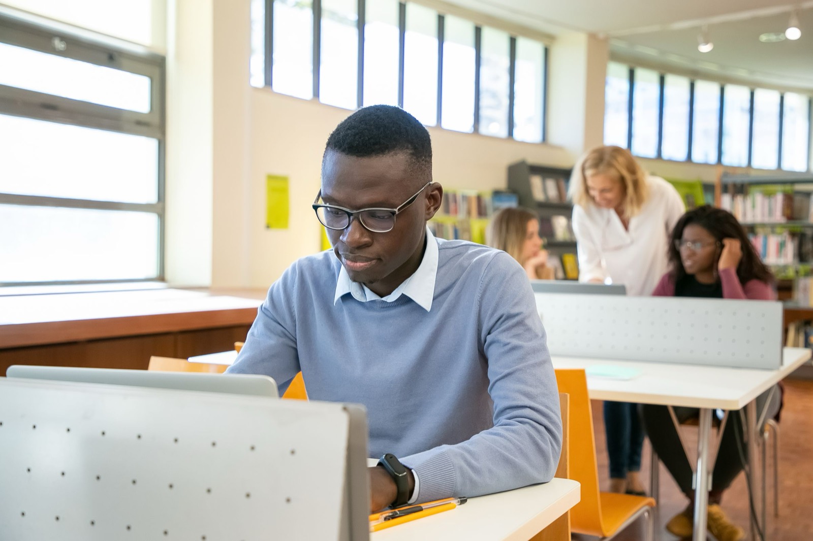 Young man in glasses working on a laptop at a desk in a bright university library